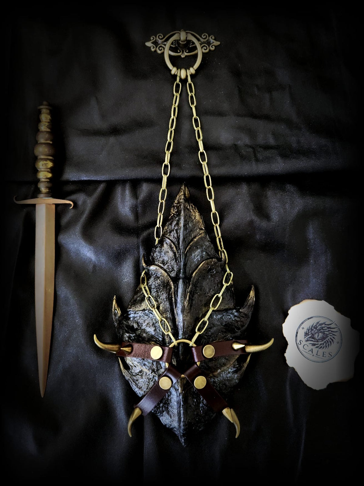 Écaille de Tairn entièrement sculptée et peinte à la main, présentée avec son harnais artisanal en cuir de vachette et chaîne dorée.