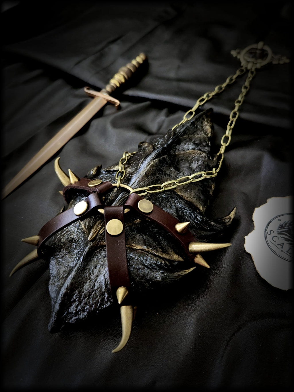 Écaille de Tairn entièrement sculptée et peinte à la main, présentée avec son harnais artisanal en cuir de vachette et chaîne dorée.